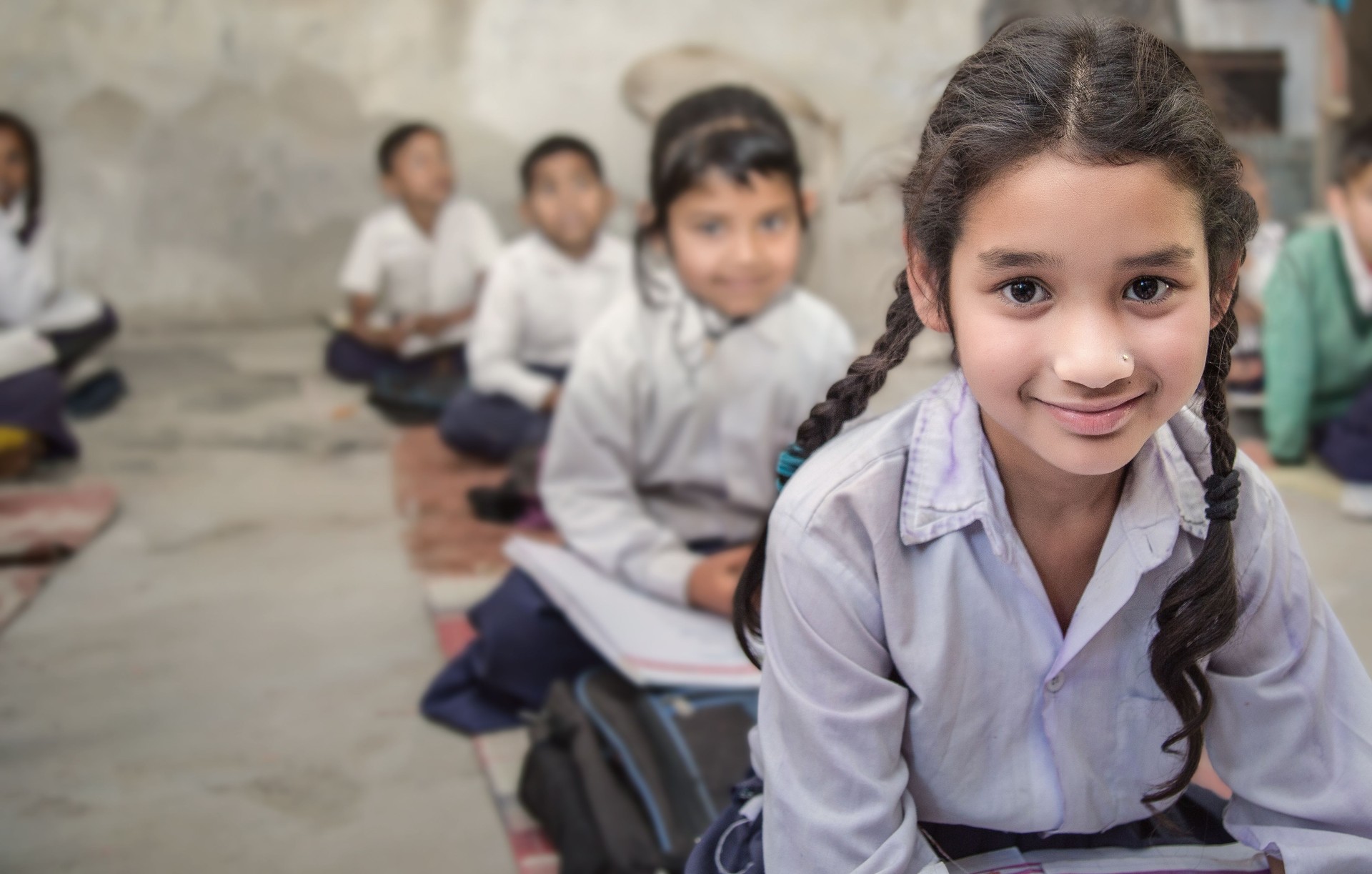 School girl in uniform of Indian Ethnicity sitting in their village classroom, looking at camera smiling.